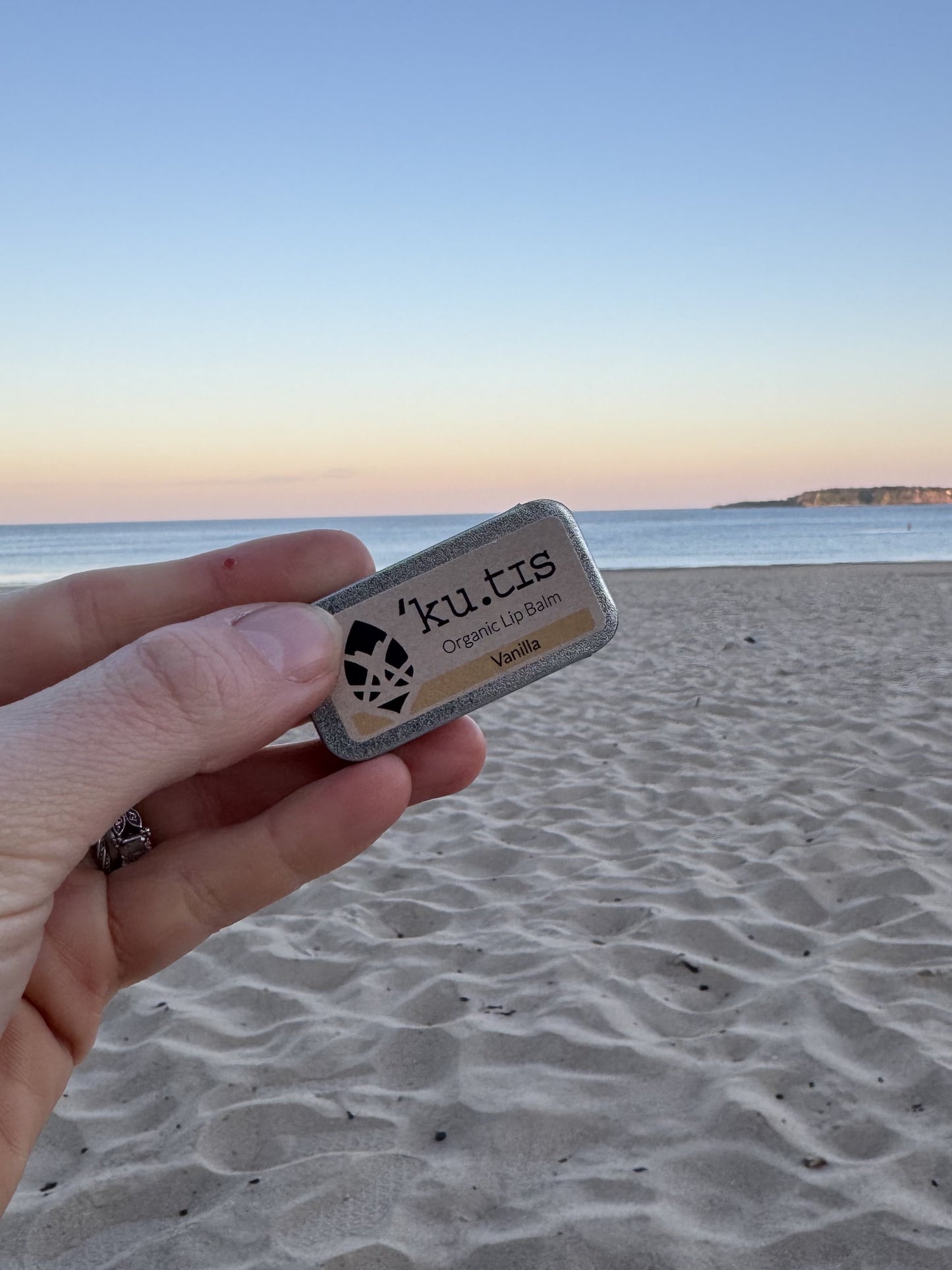 A lipbalm by local Welsh maker, surrounded by sand and gentle waves in the background.