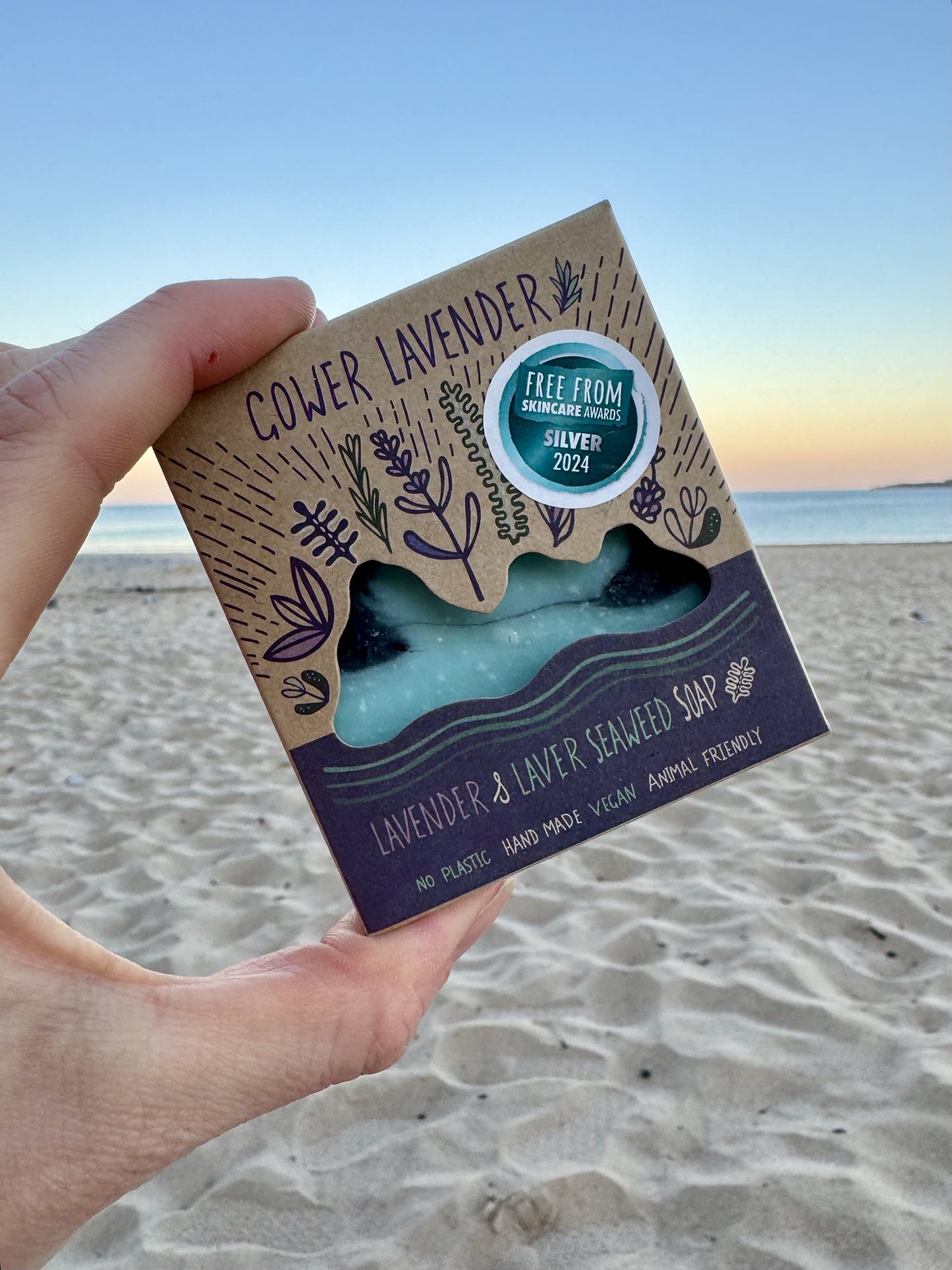 Lavender and Laver Seaweed soap by local Welsh maker, surrounded by sand and gentle waves in the background.