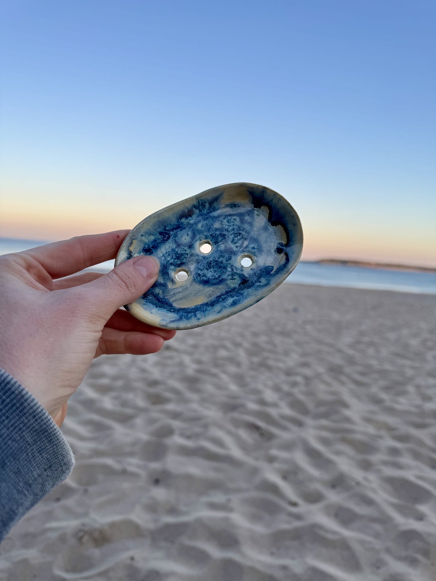 Ceramic soap dish by local Welsh maker, surrounded by sand and gentle waves in the background.