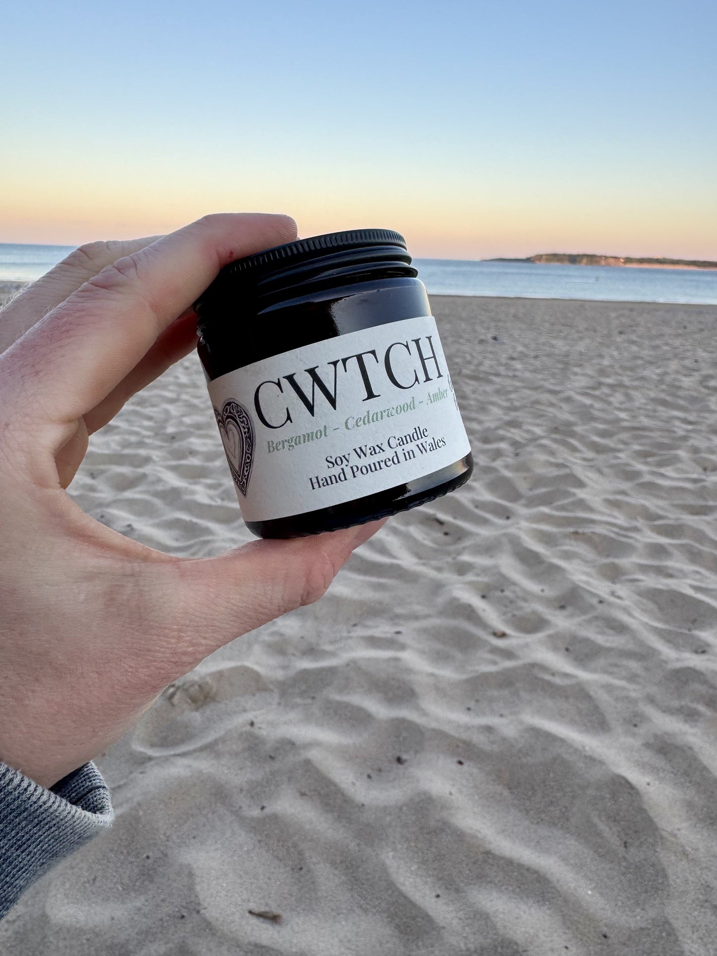 Candle by local Welsh maker, surrounded by sand and gentle waves in the background.