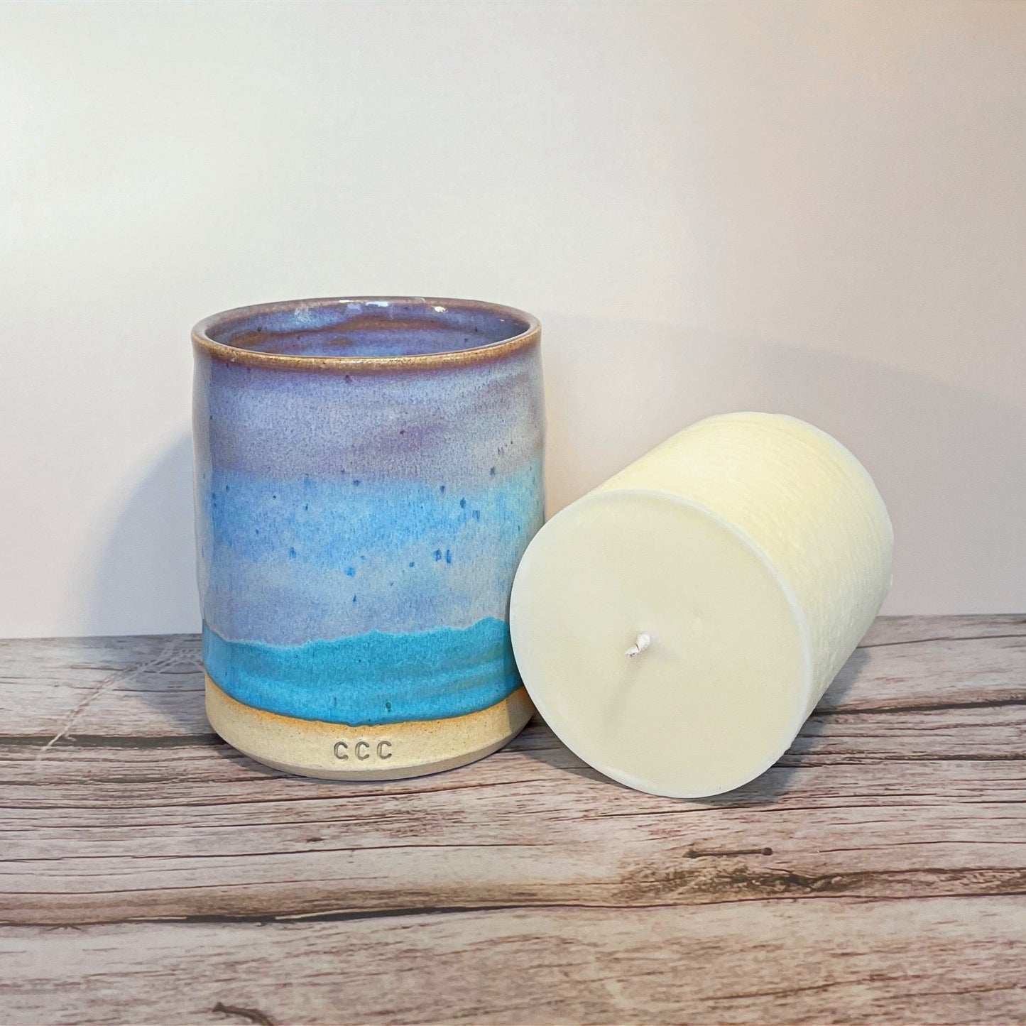 A refillable candle in a blue and purple ceramic pot, showcasing its elegant design inspired by mermaids. Sat next to a white candle. Perfect for gifts or for enjoying moments at home.