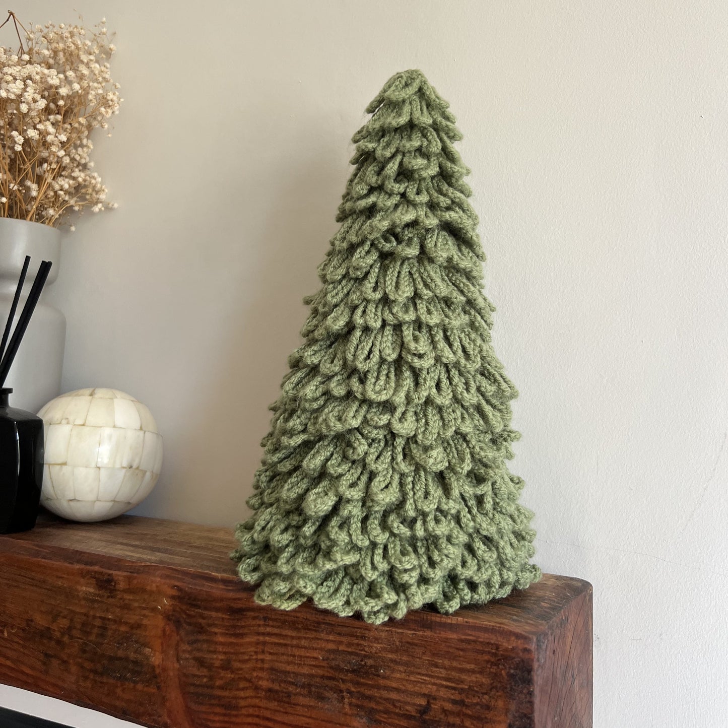 Handmade sage green crocheted Christmas tree ornament on a wooden surface with a neutral background