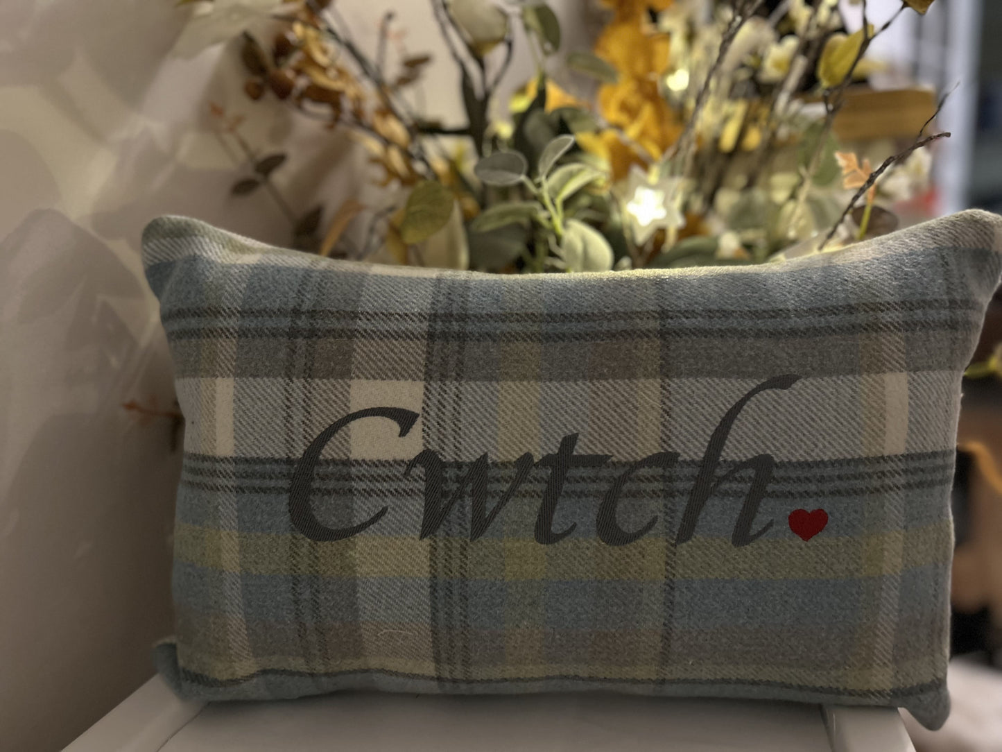 Plaid pillow with 'Cwtch' and a heart on a decorative background