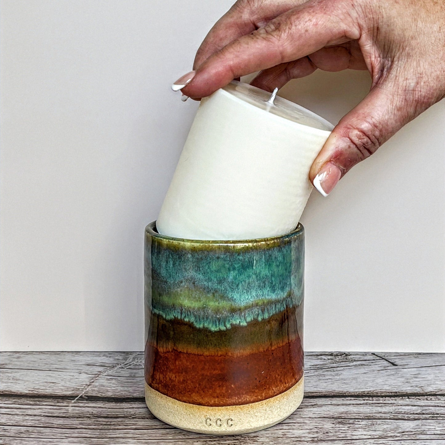 A refillable candle in a decorative green and brown ceramic pot, showcasing its elegant design and warm glow. Perfect for gifts or for enjoying moments at home.