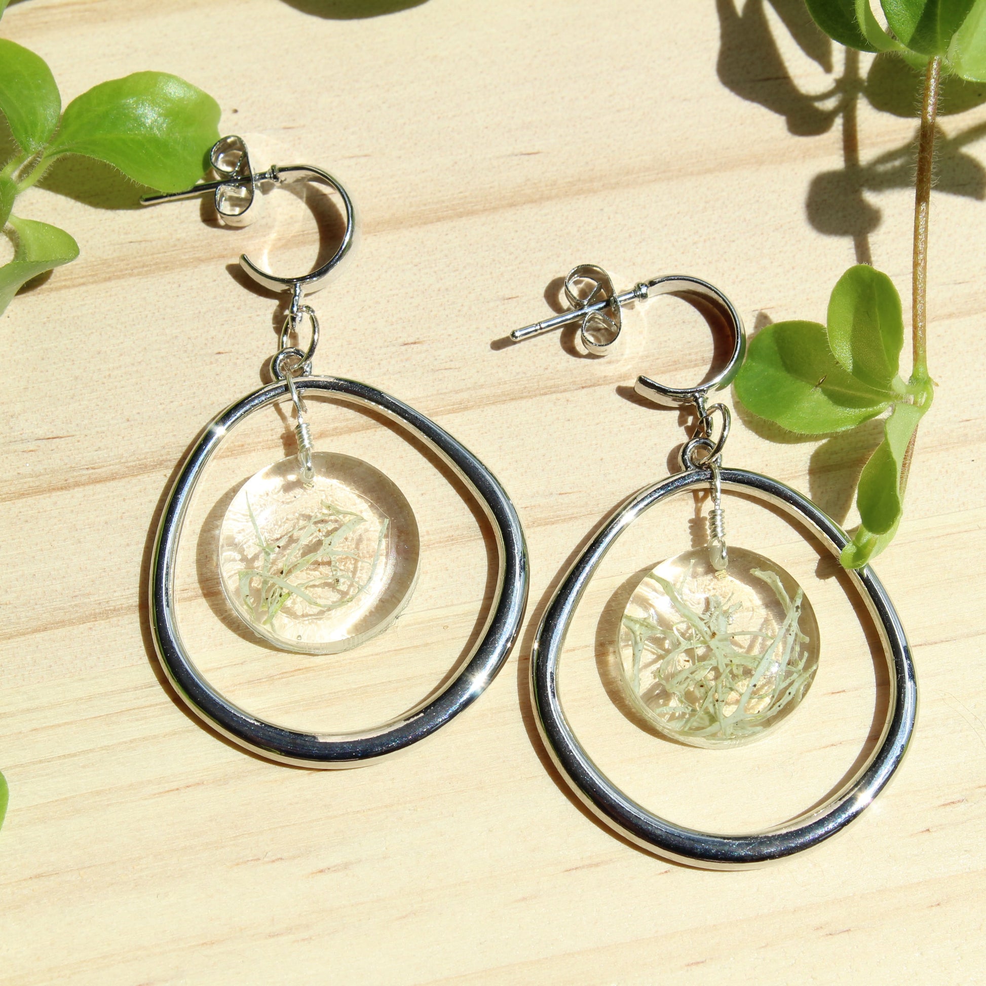 Silver hoop earrings with circular designs on a wooden surface with green leaves. Perfect gift for jewellery lovers, sustainable style seekers, or anyone who loves bold, handmade accessories