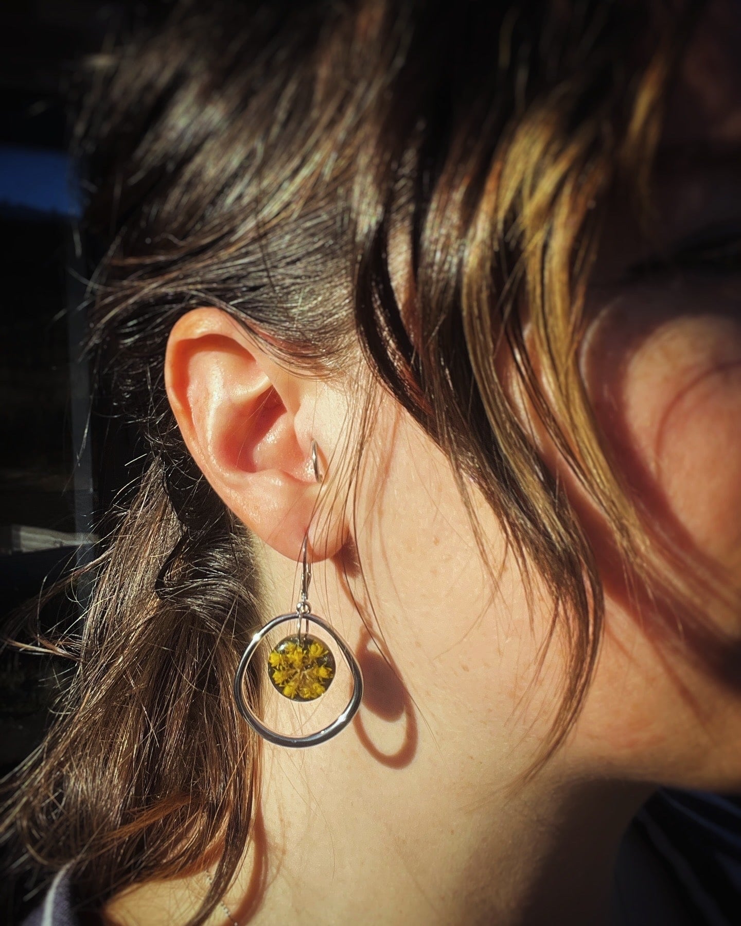 Close-up of an earring with a yellow gemstone worn by a person.