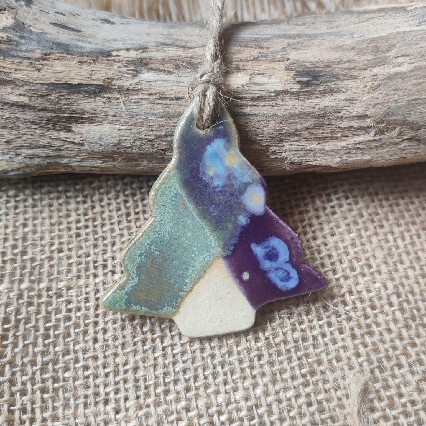 Colourful green blue handmade ceramic christmas tree ornament hanging on a string against a rustic background. Perfect handmade gift for christmas, made in wales.