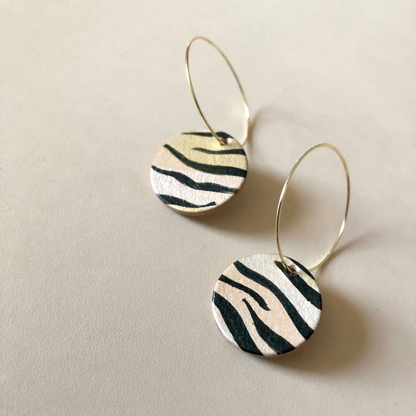 Close-up of handmade tiger patterned leather hoop earrings on gold-plated hoops.