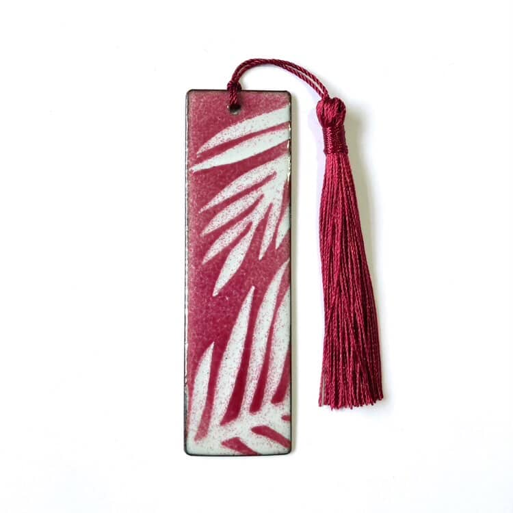 Bookmark with red and white leaf pattern and tassel on a white background. Handmade enamelled copper finish, made in Wales.