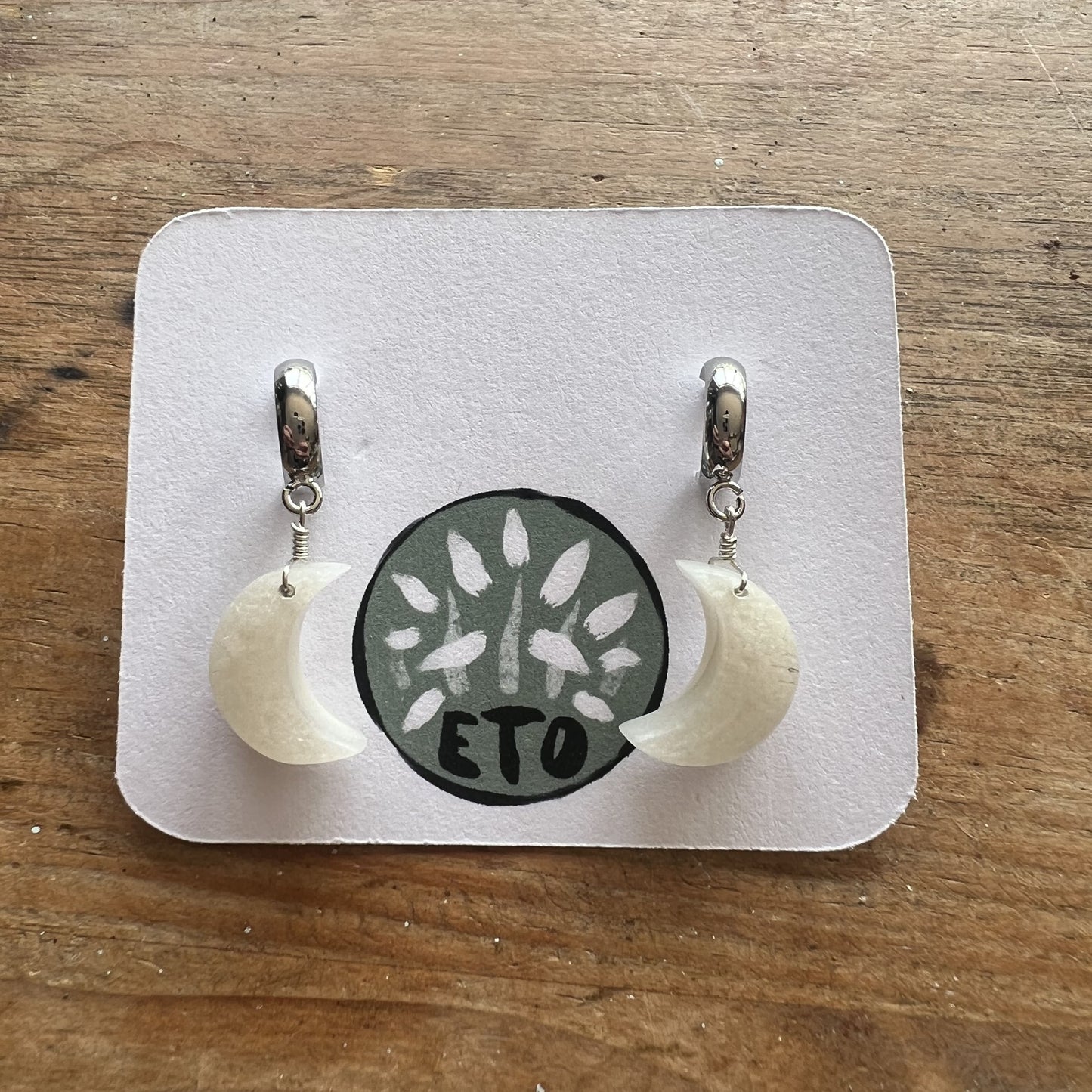 Pair of moon shaped earrings on a display card with, elegantly crafted for a unique accessory choice, on a wooden surface
