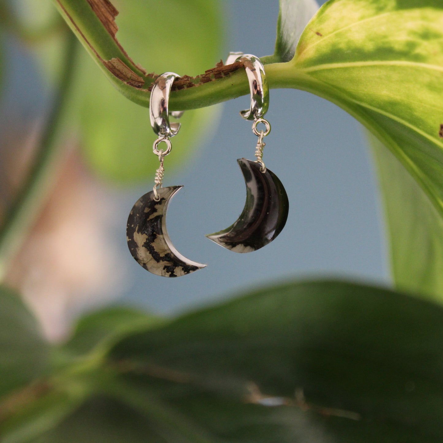Crescent moon-shaped earrings hanging on a leaf with a natural background