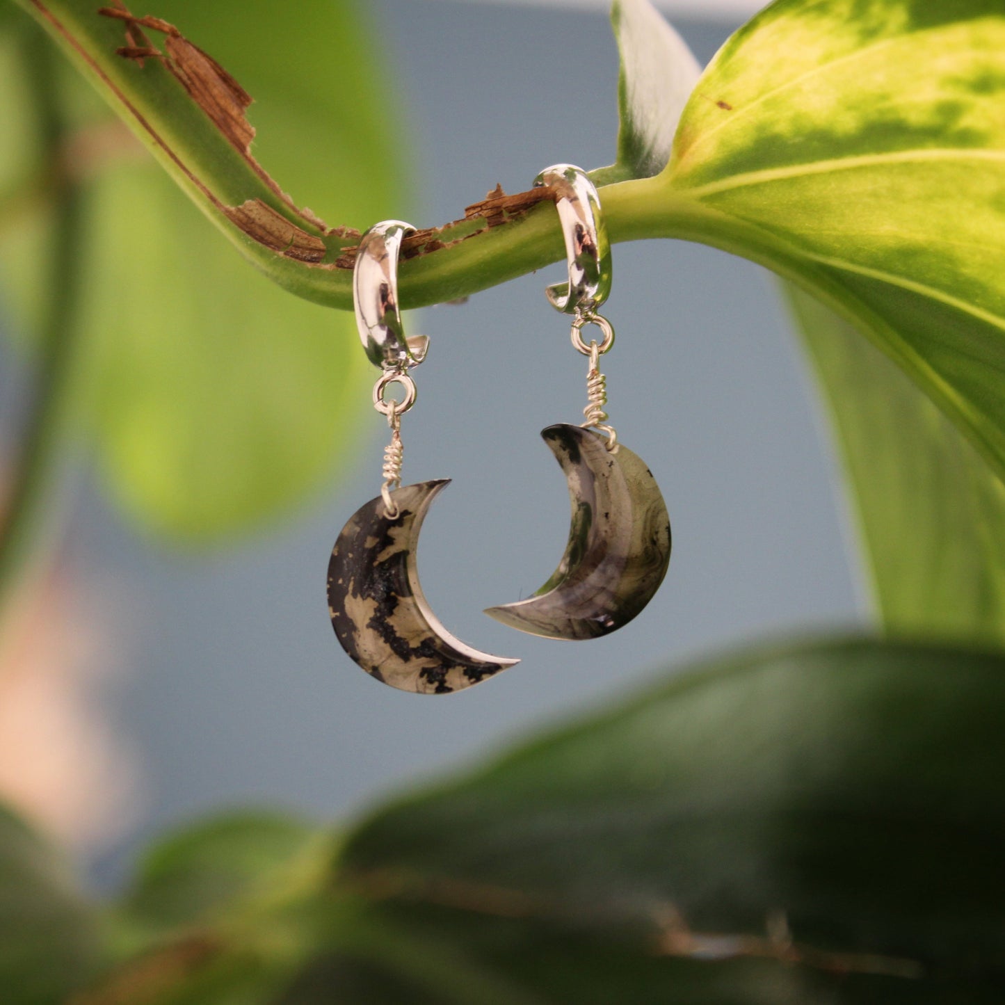 Crescent moon-shaped earrings hanging on a leaf with a blurred natural background