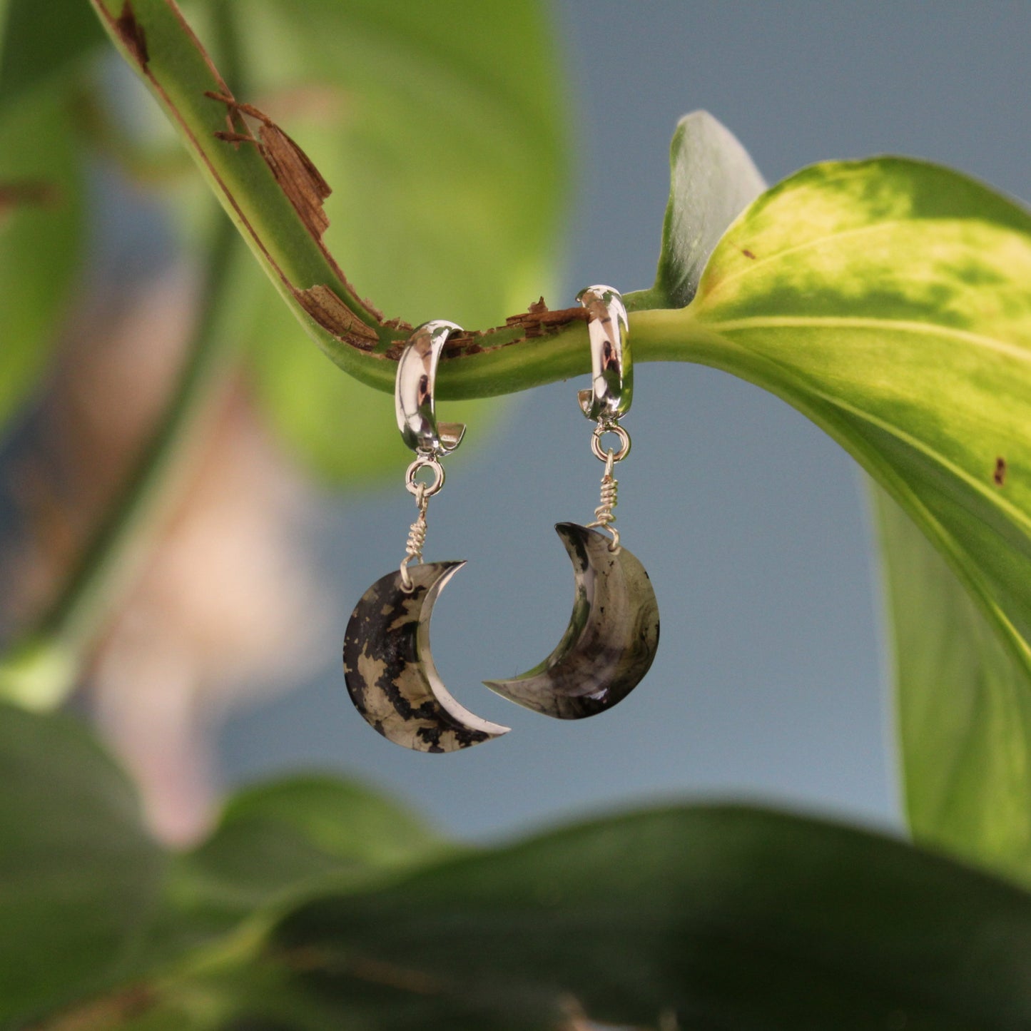 Crescent moon-shaped earrings hanging on a leaf with a blurred background
