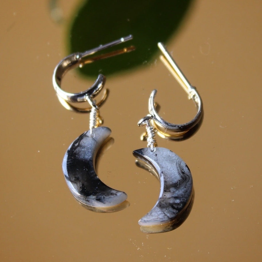 Moon-shaped earrings on a reflective surface with a brown background.