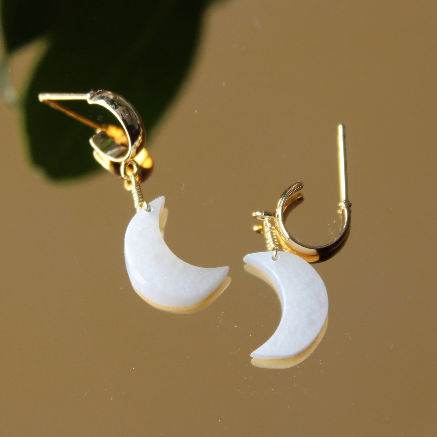 Gold earrings with white crescent moon charms on a brown background
