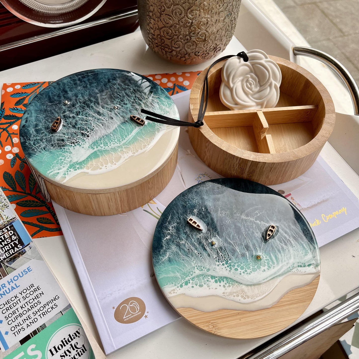 Wooden containers with ocean wave design lids on a surface with magazines.