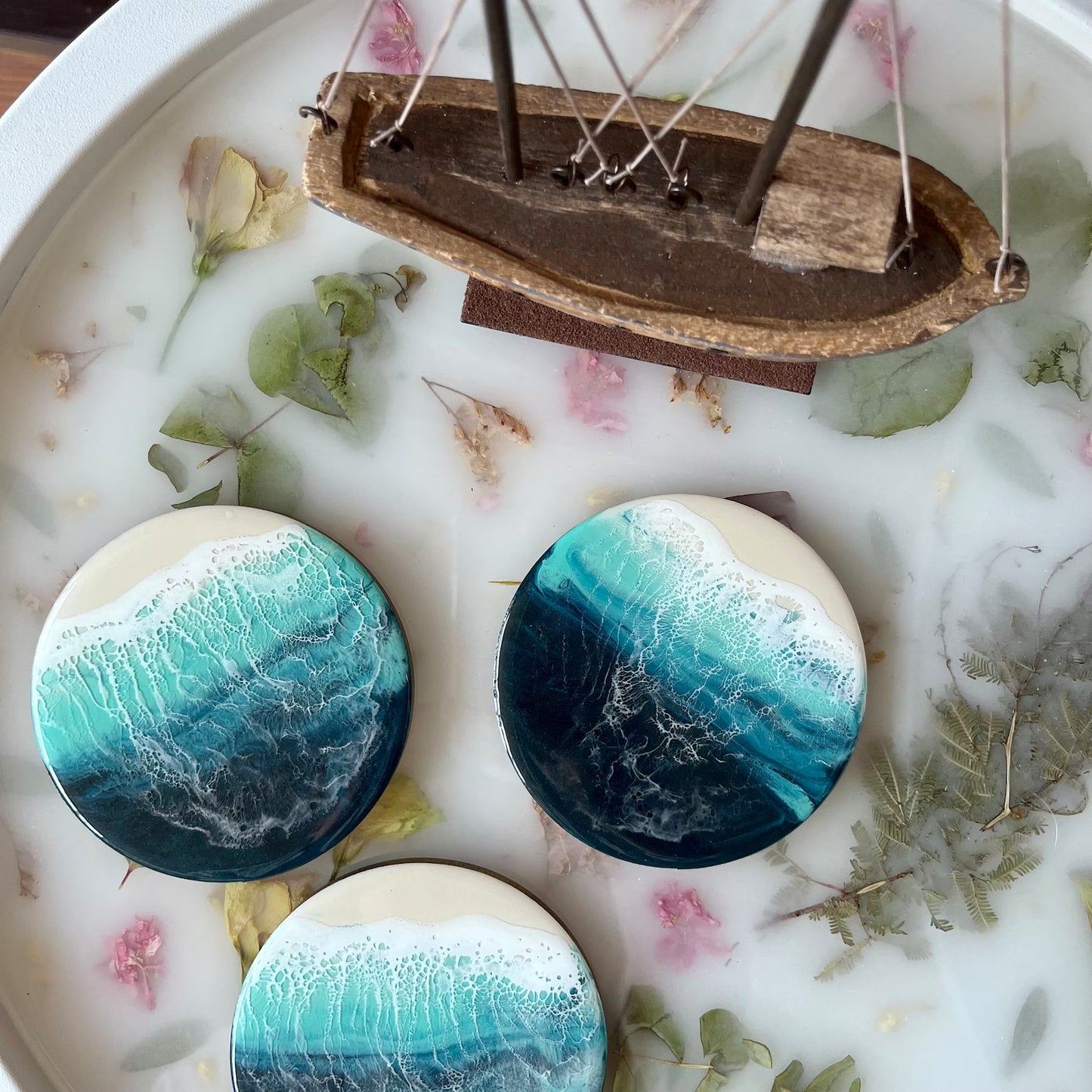 Three circular blue and white ceramic pieces with a small wooden boat on a decorative surface with leaves and flowers.