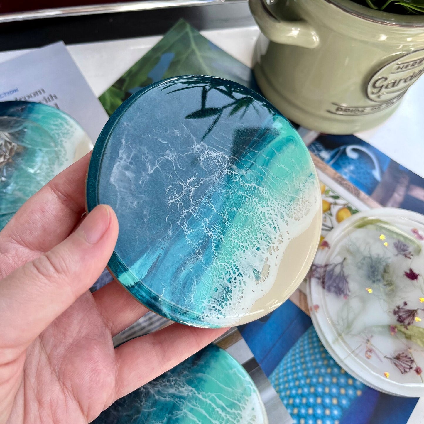Hand holding a blue and green marbled coaster with a blurred background