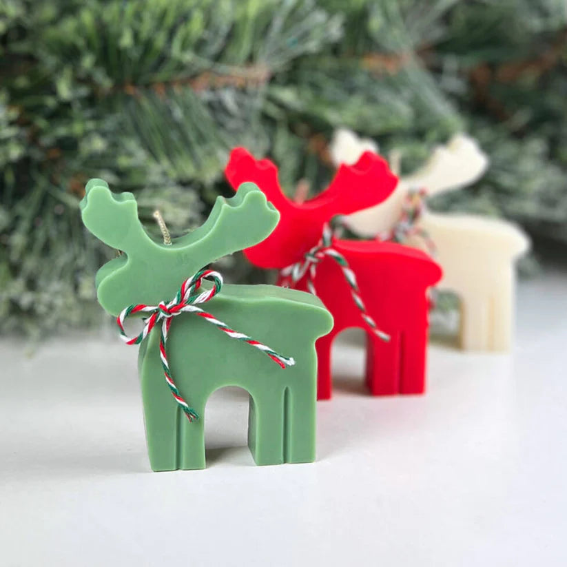 Green and red reindeer-shaped candles with a Christmas tree in the background