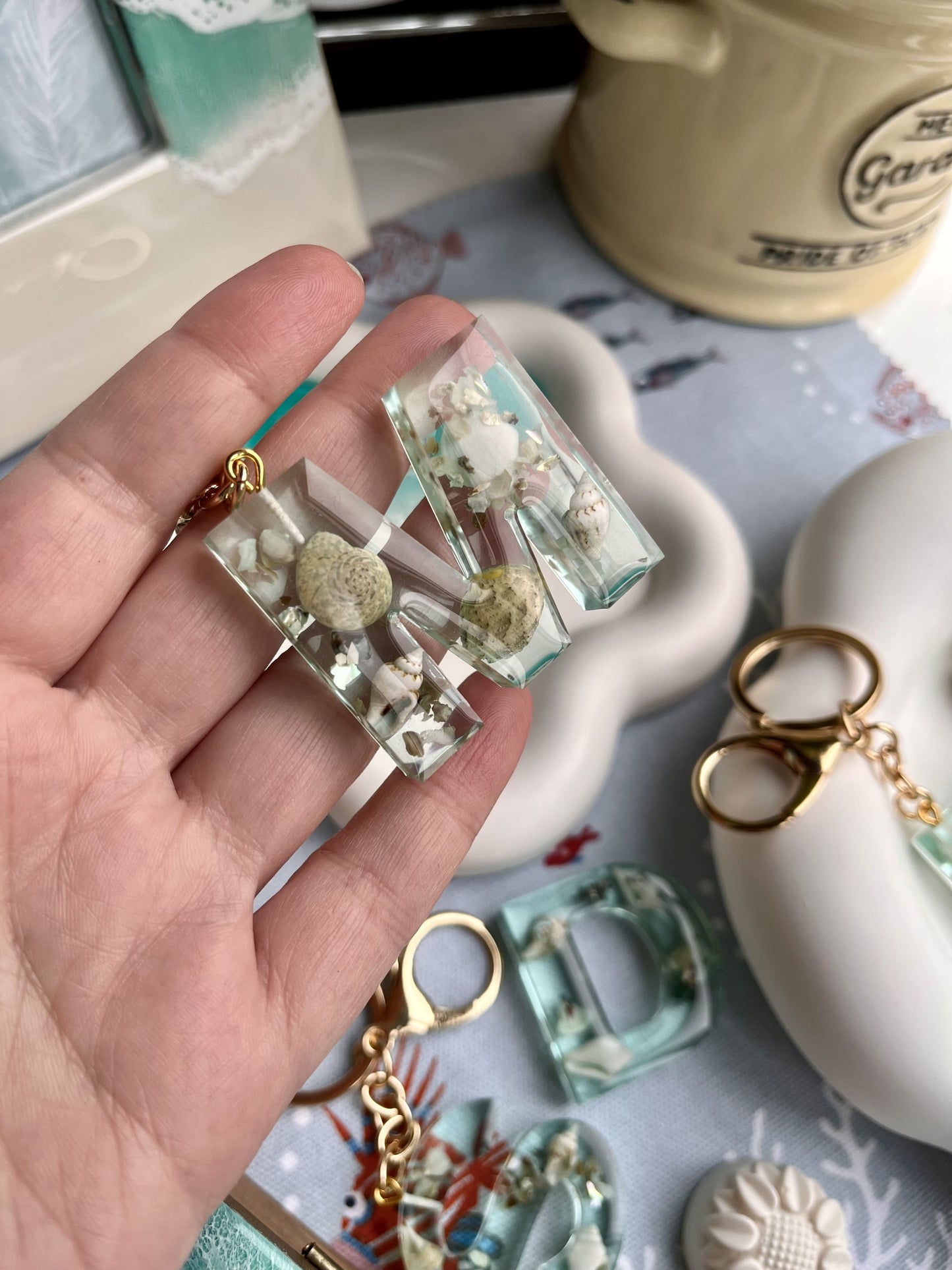 Hand holding a clear resin keychain with embedded seashells and gold accents on a decorative surface.