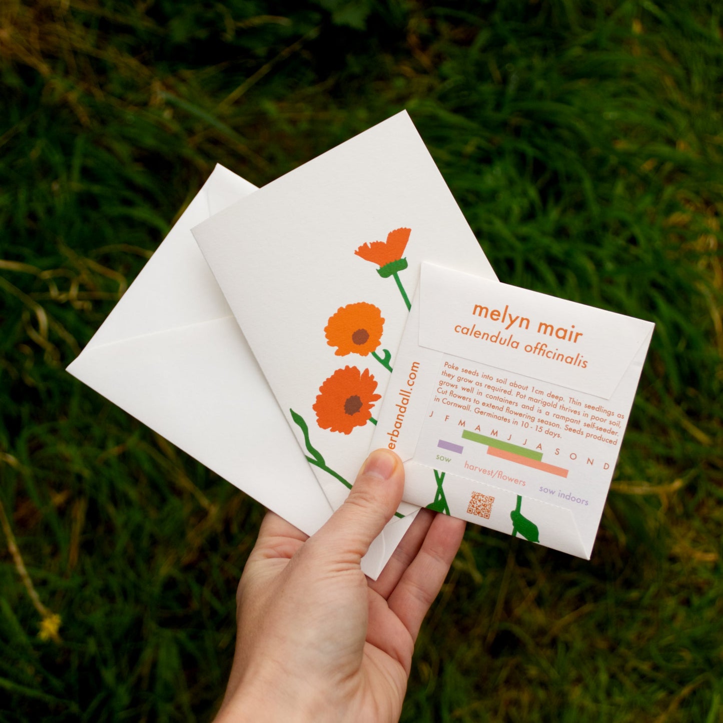 Hand holding a card with floral design and text on a grassy background