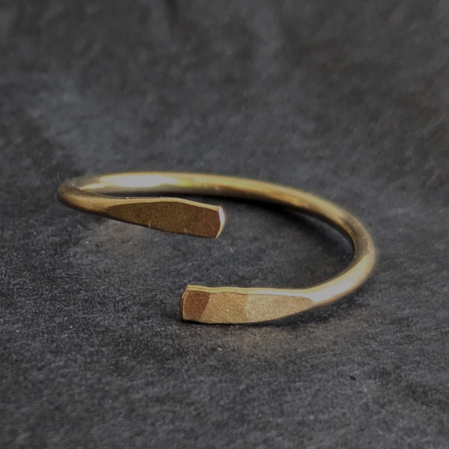 Gold adjustable smooth ring sat on slate background. 