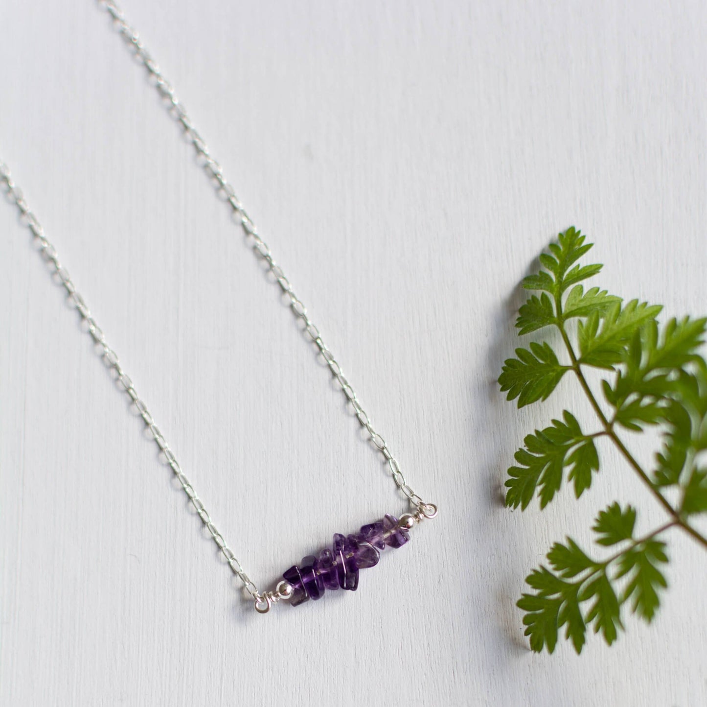 Purple Amethyst Crystals Necklace on silver chain, sat on grey background