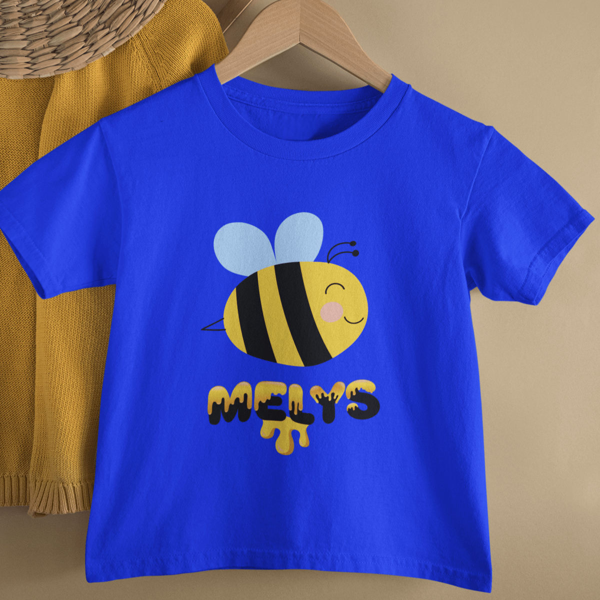 A kids' t-shirt featuring an illustrated bee design, hung up on a wooden hanger. Perfect for new baby and toddler gifts, birthdays, school days, playtime or thoughtful Welsh gifts for children.