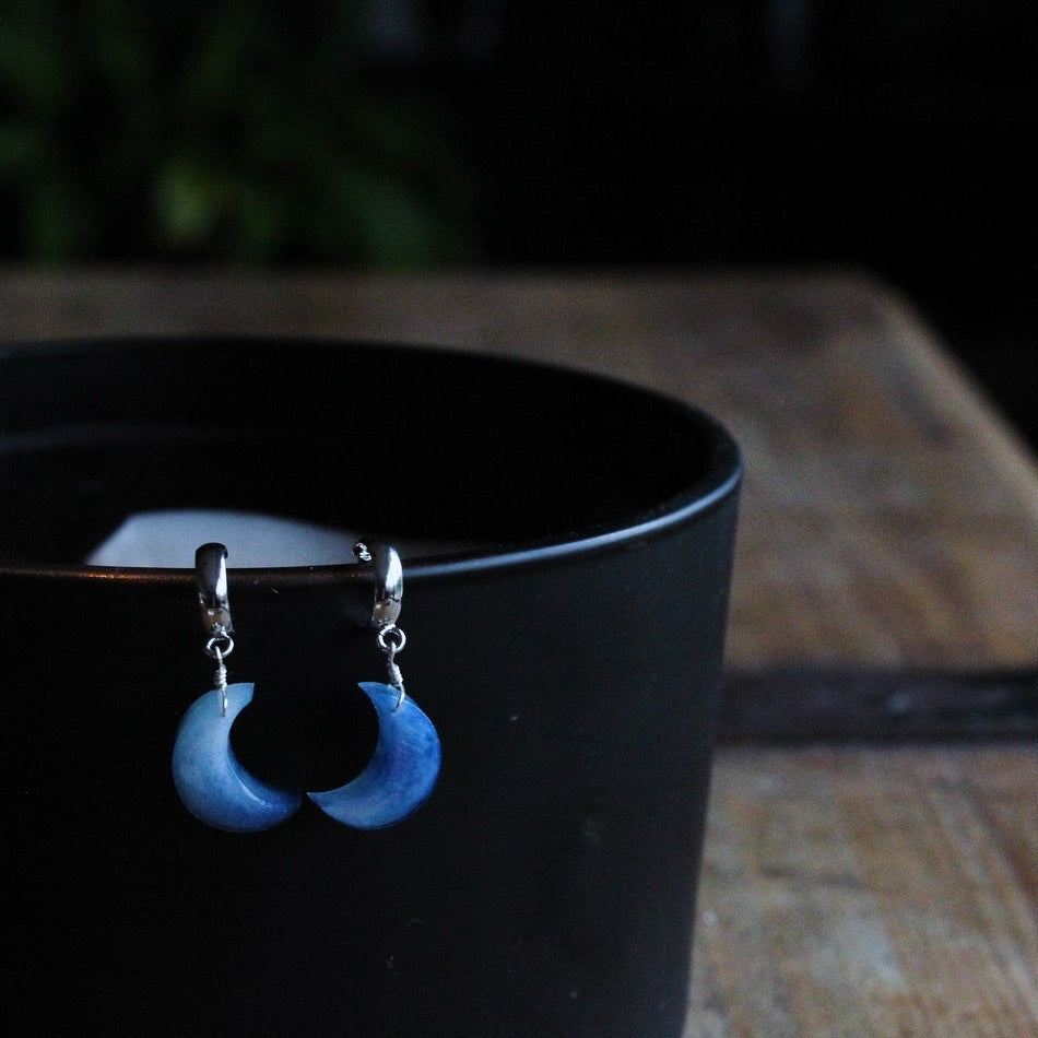 Blue handmade resin earrings on a black cup with a blurred background, made in Wales. Perfect gift for her.