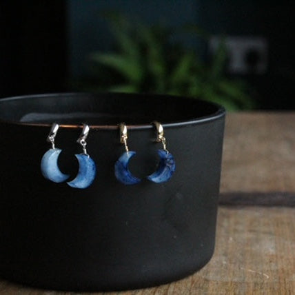 Blue handmade marble resin moon-shaped earrings on a black stand with a blurred background