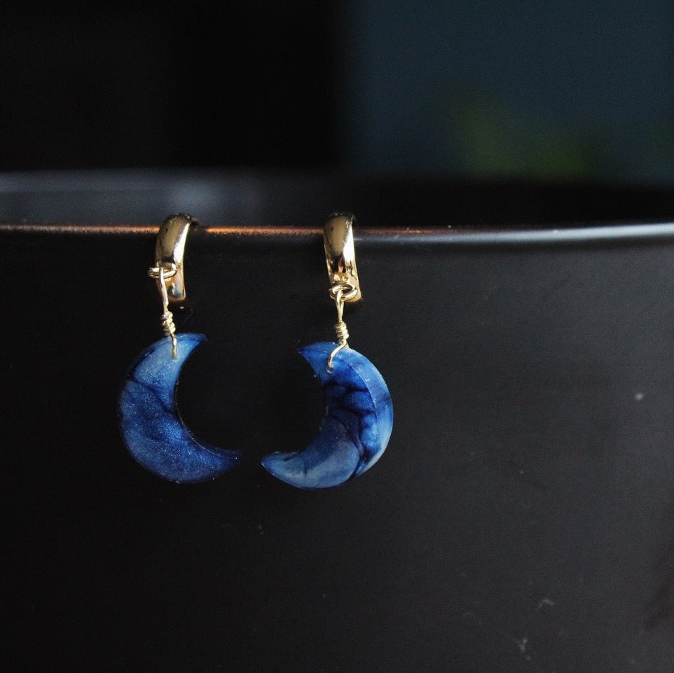 Blue handmade resin crescent moon earrings on a black surface with a blurred background, perfect gift for her.