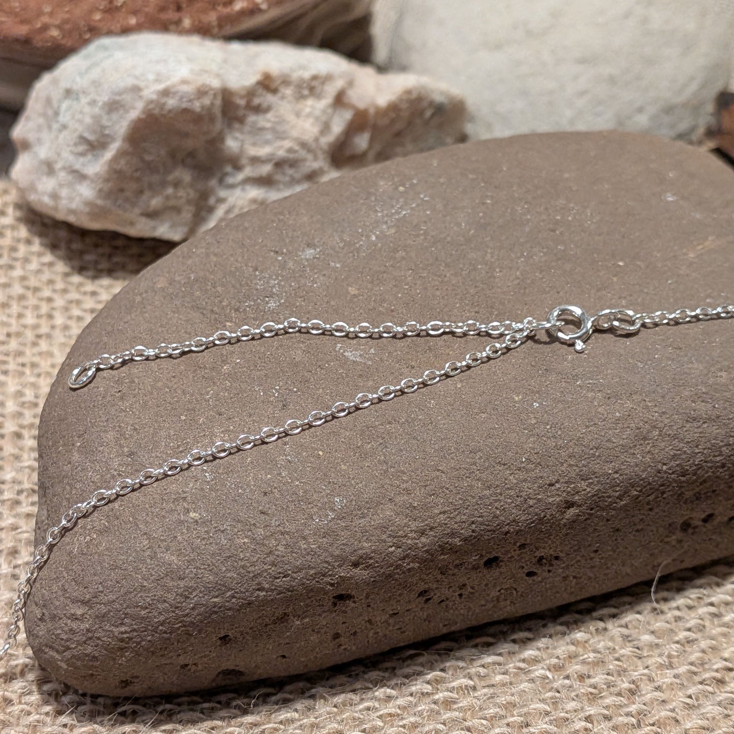 Nature inspired Welsh silver jewellery, Brynniau hills and sun pendant. Showcasing the silver chain on a stone background.