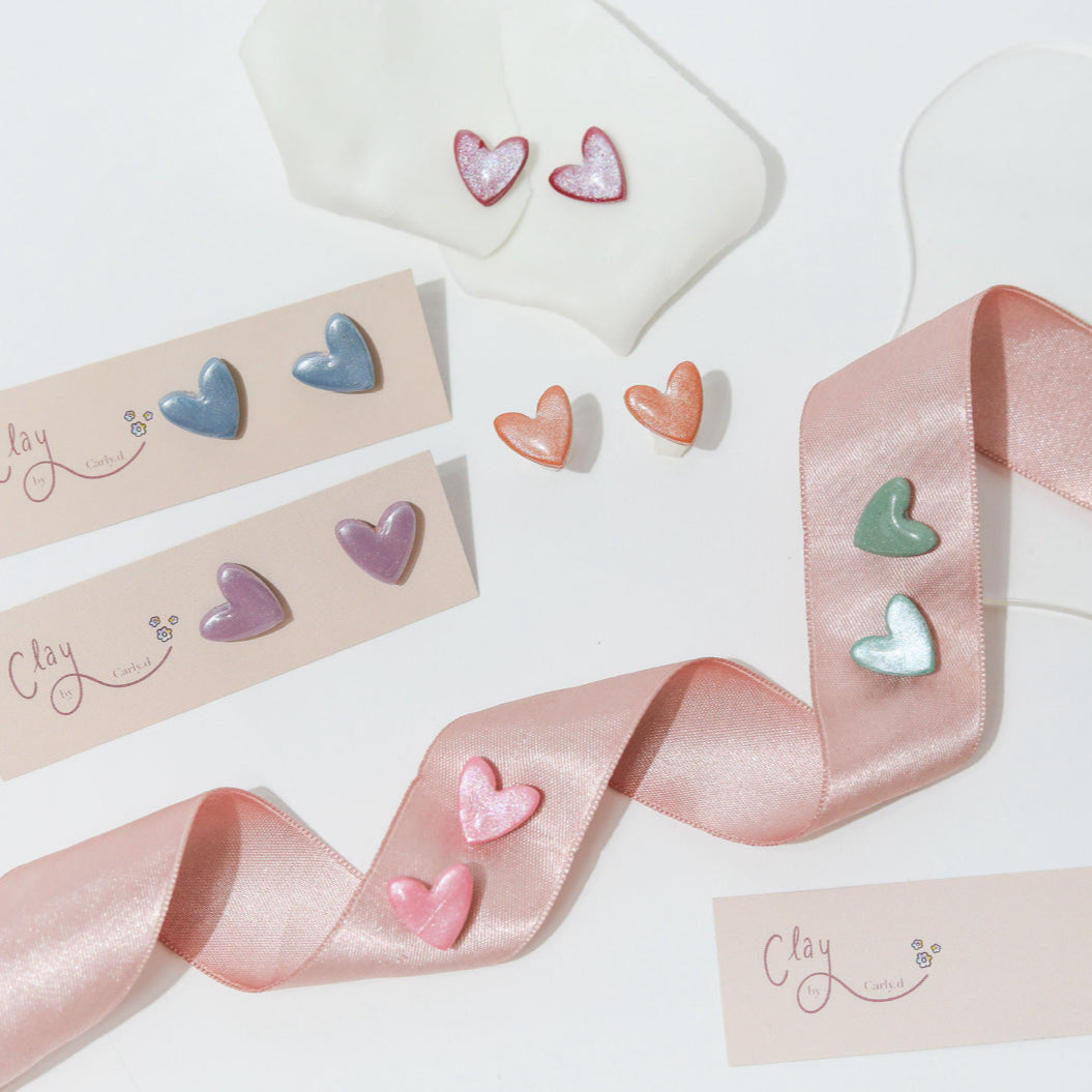 Multiple sets of colourful heart shape stud earrings, layered on pink ribbons. Making a lovely gift for her or a treat for yourself. Ideal for lovers of bold jewellery, playful accessories and handmade gifts that add a pop of personality.