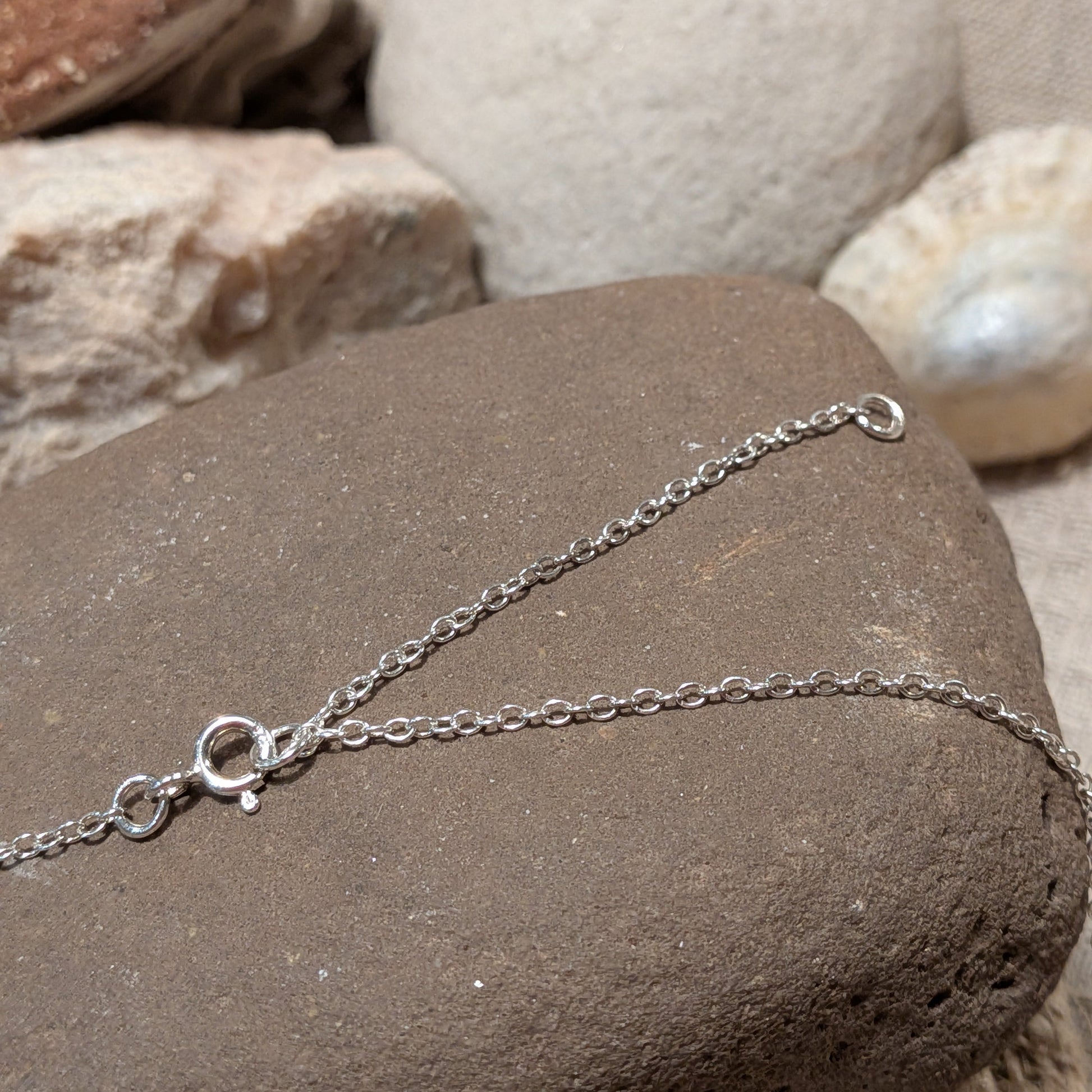 Dydd-Ton silver wave scene necklace handmade in Wales with sun, cloud and wave design. Image shows chain on a stone rock.