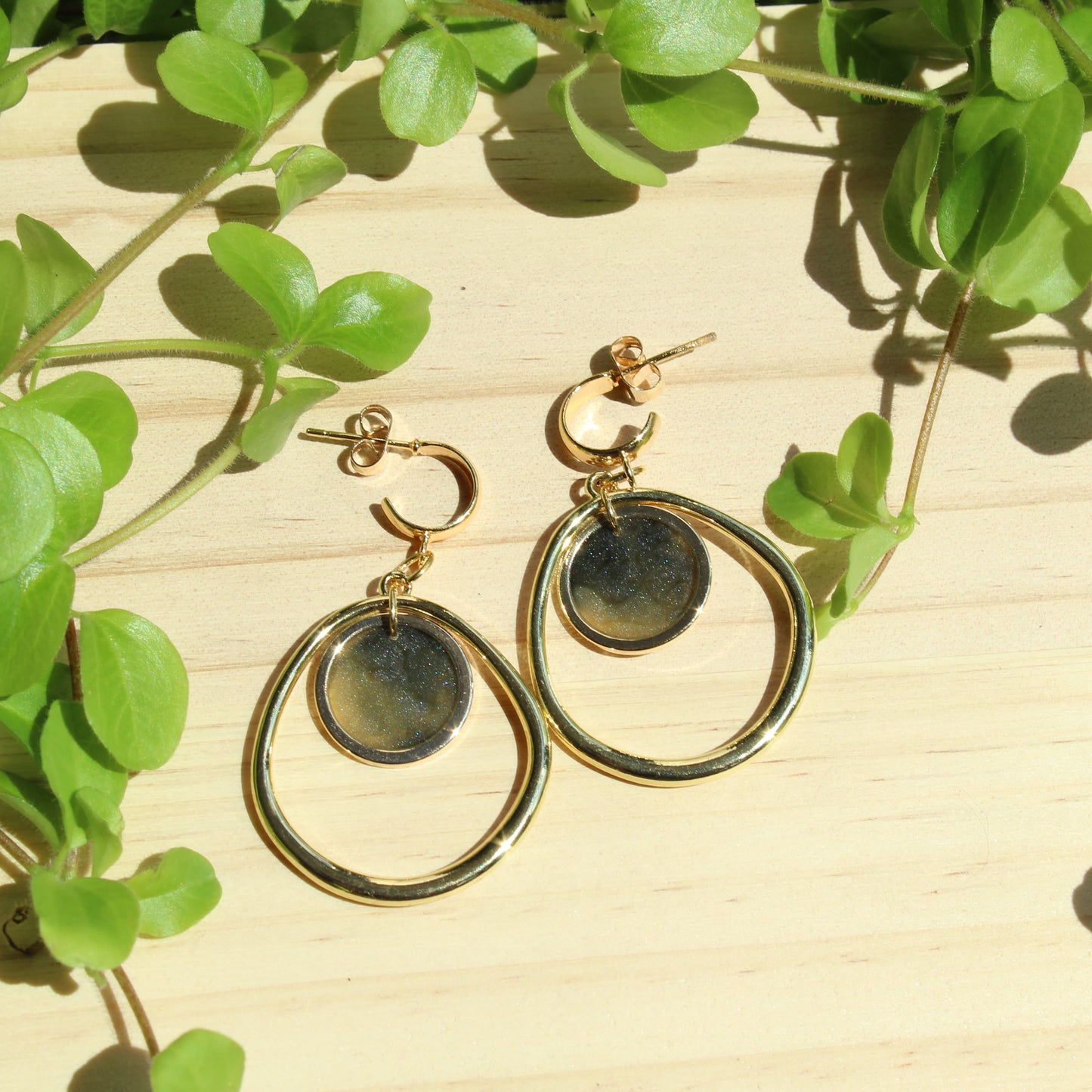 Gold hoop earrings on a wooden surface with green leaves