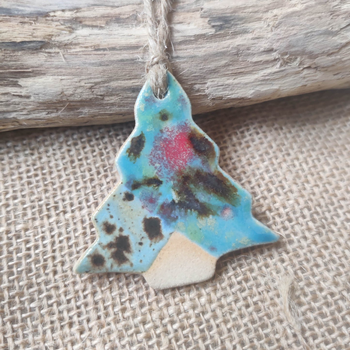 Colourful blue green pink handmade ceramic christmas tree ornament on a string against a rustic wooden and burlap background. Perfect for christmas gifts, supporting local handmade makers in wales.