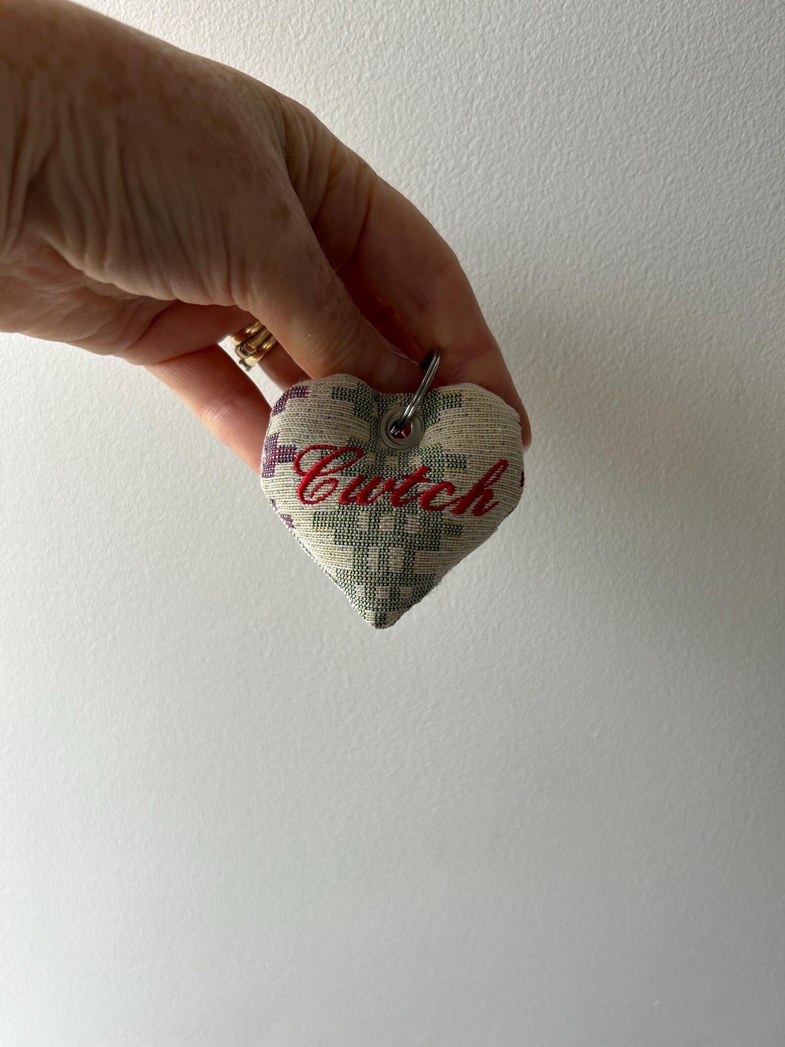 Handmade heart-shaped fabric keyring with 'Cwtch' embroidered text. Held by a hand against a white background. unique Welsh textile gift accessory for birthdays, Christmas, weddings