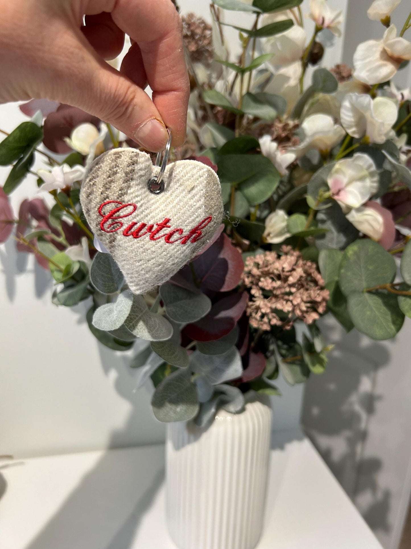Handmade heart-shaped keychain with 'Cwtch' text held over a floral arrangement.  unique Welsh textile gift accessory for birthdays, Christmas, weddings