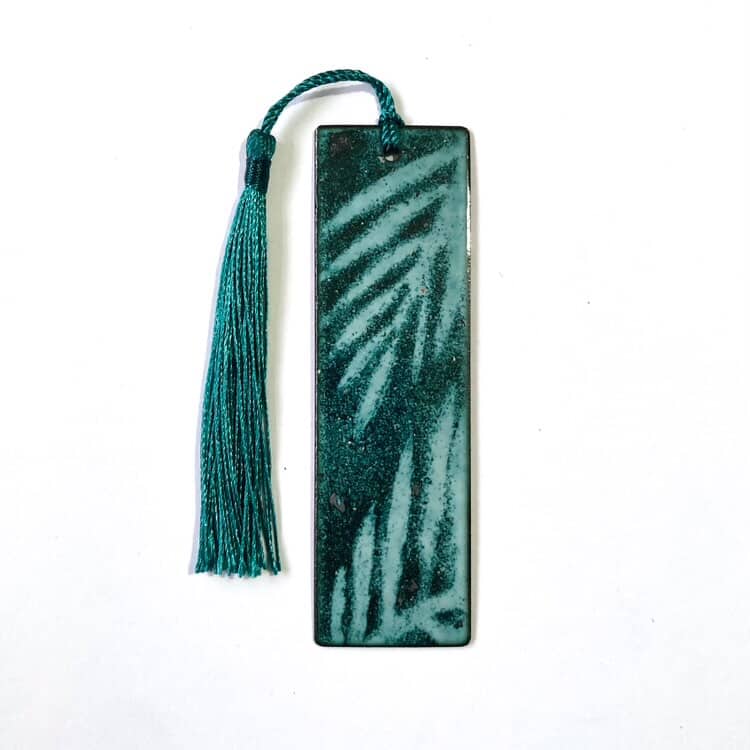 Handmade enamelled copper bookmark in green finish with leaf pattern and tassel on a white background. Perfect gift from Wales.