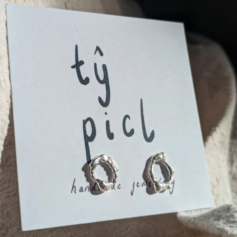 Silver textured circular earrings sat on a card backing