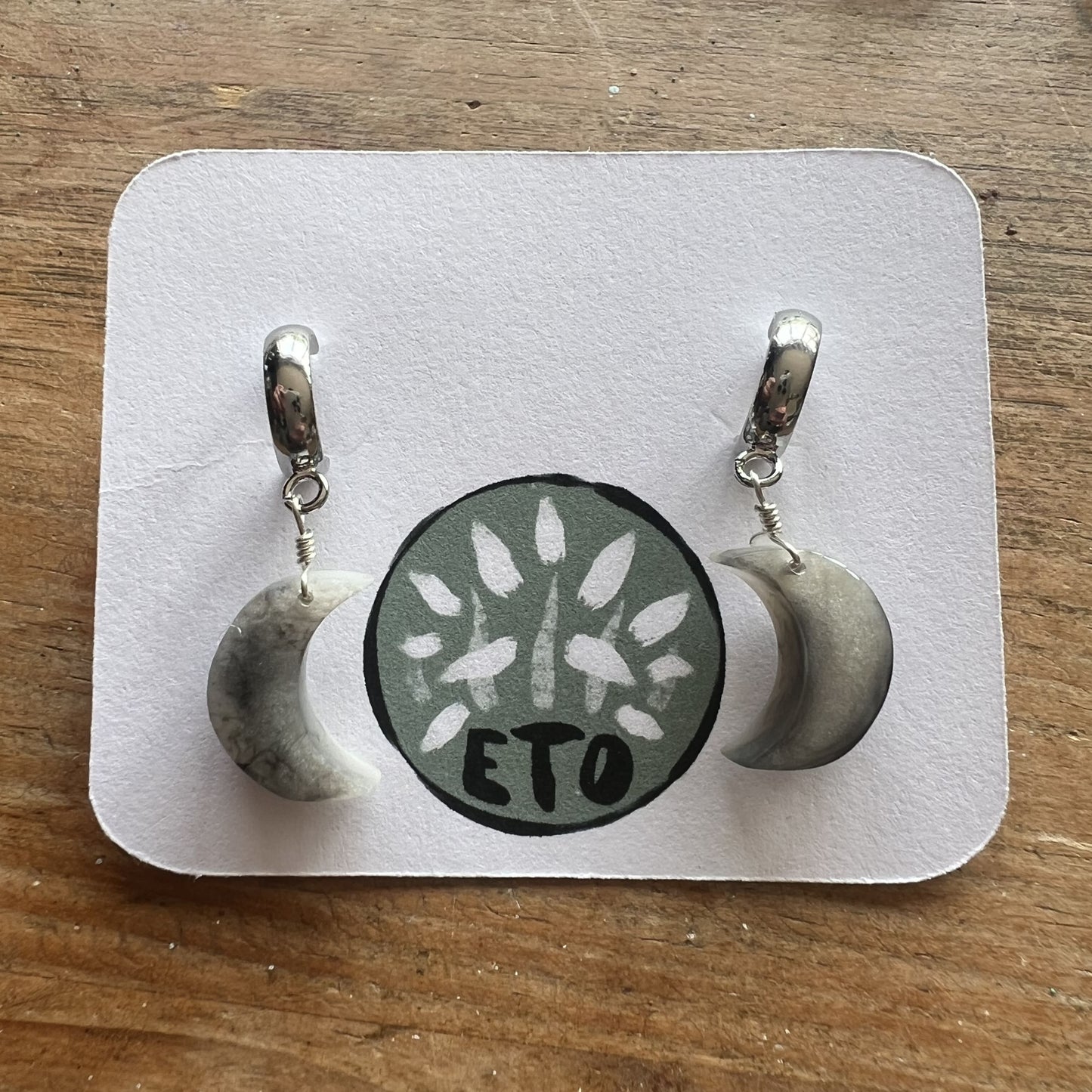 Pair of earrings on a display card with 'ETO' branding on a wooden surface