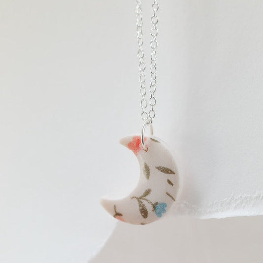 Small white and pink crescent necklace featuring floral designs made of polymer clay and resin. Ideal for gifts for her, lovers of bold jewellery, floral prints and handmade artisan gifts.