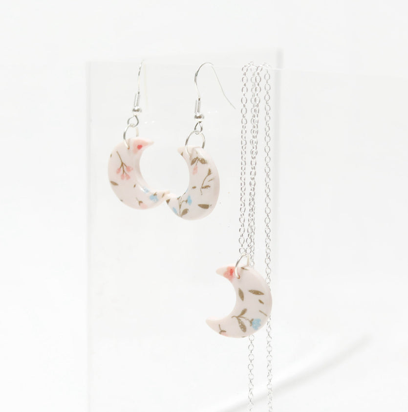 Small white and pink crescent necklace featuring floral designs made of polymer clay and resin. Ideal for gifts for her, lovers of bold jewellery, floral prints and handmade artisan gifts.
