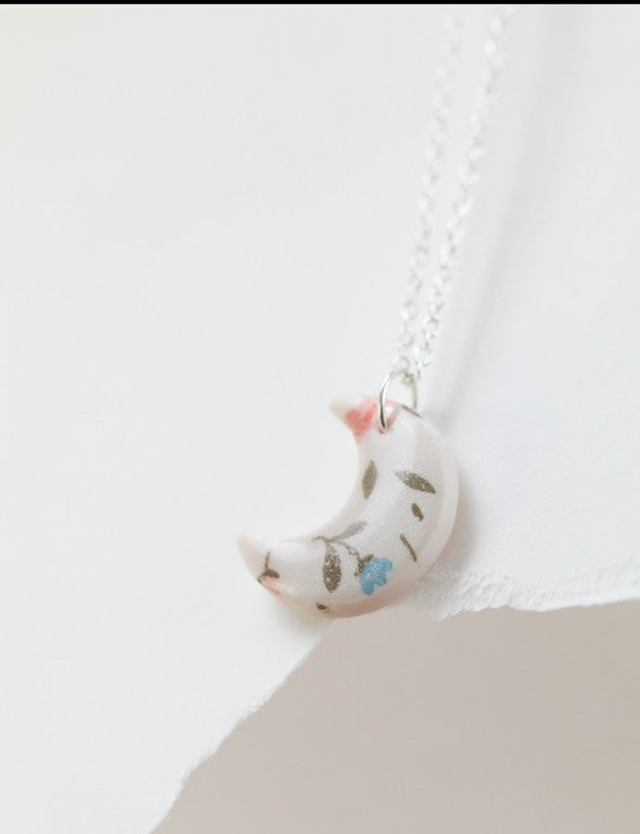 Small white and pink crescent necklace featuring floral designs made of polymer clay and resin. Ideal for gifts for her, lovers of bold jewellery, floral prints and handmade artisan gifts.