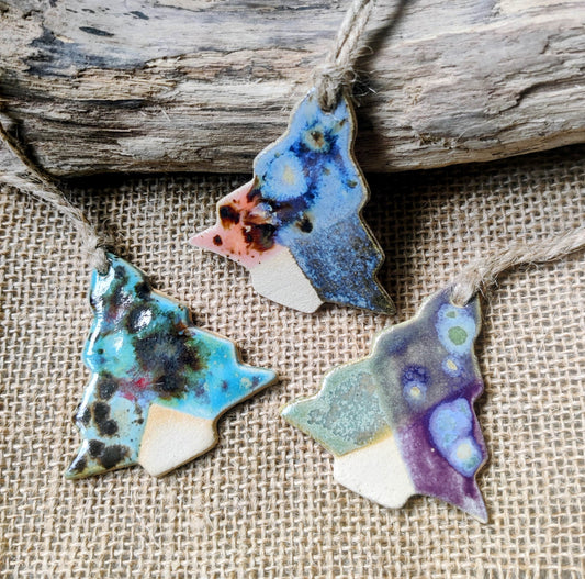 Three colourful ceramic tree shaped ornaments in blue green, hanging on a rustic wooden surface. Perfect for christmas gifts and supporting small businesses.