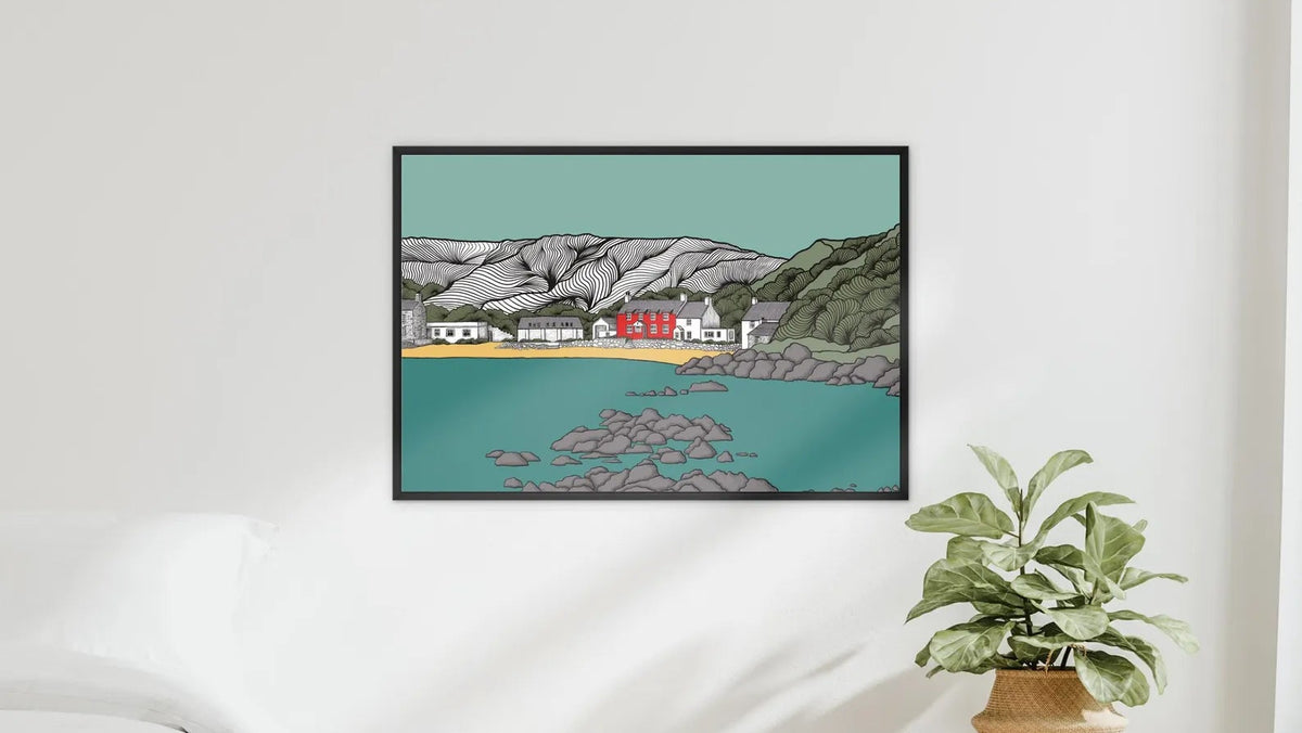 A framed art print depicting a coastal village with red houses, a sandy beach, and turquoise water, displayed on a white wall above a light wood bench with a potted plant in a styled bedroom setting.