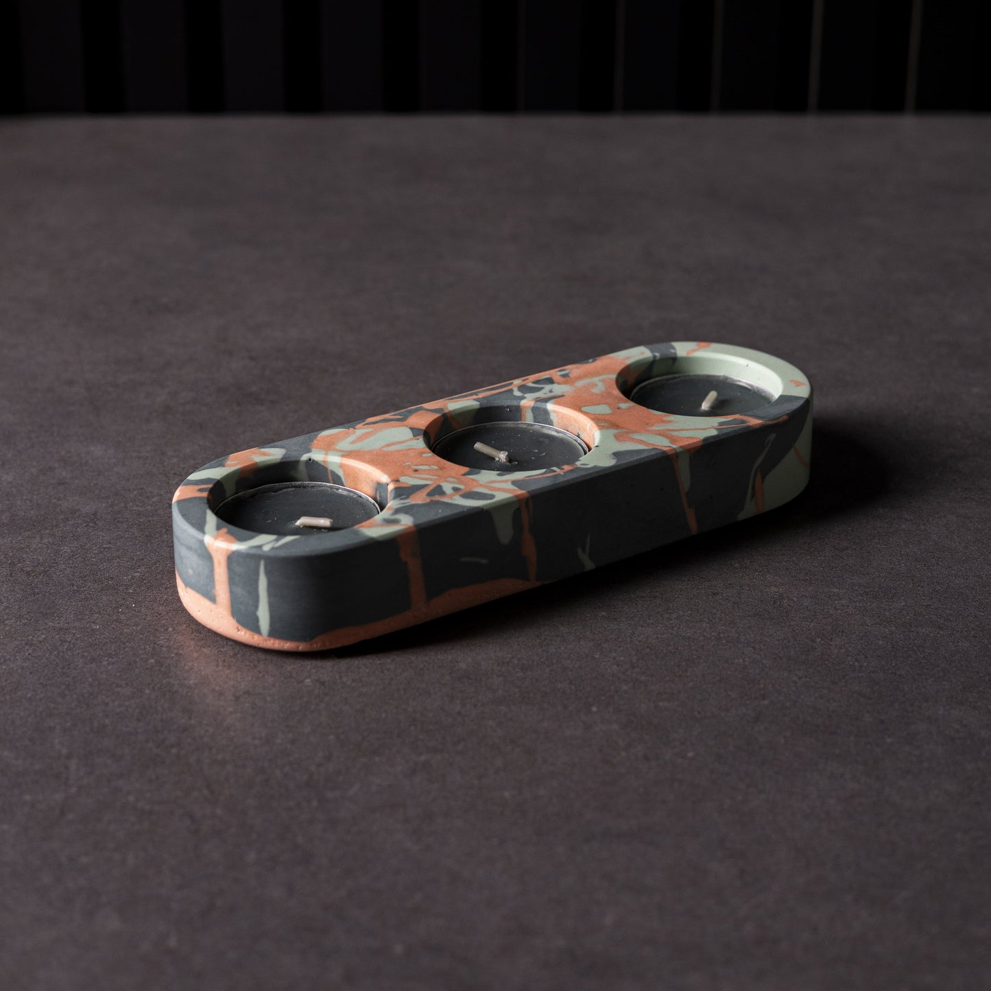 Jesmonite triple candle holder with unique splattered patterns in black, orange and green.
