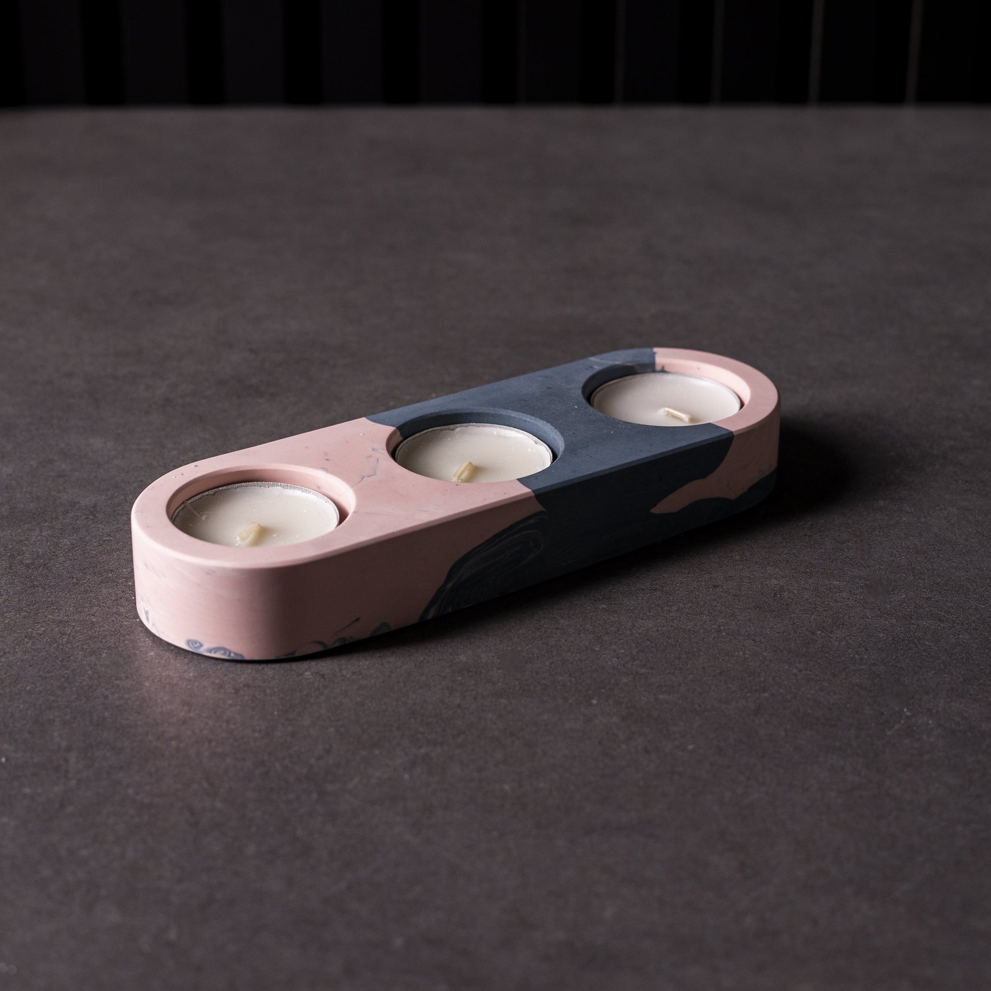 Pink and blue ceramic candle holder with three candles on a dark surface. Jesomite material, made in Wales