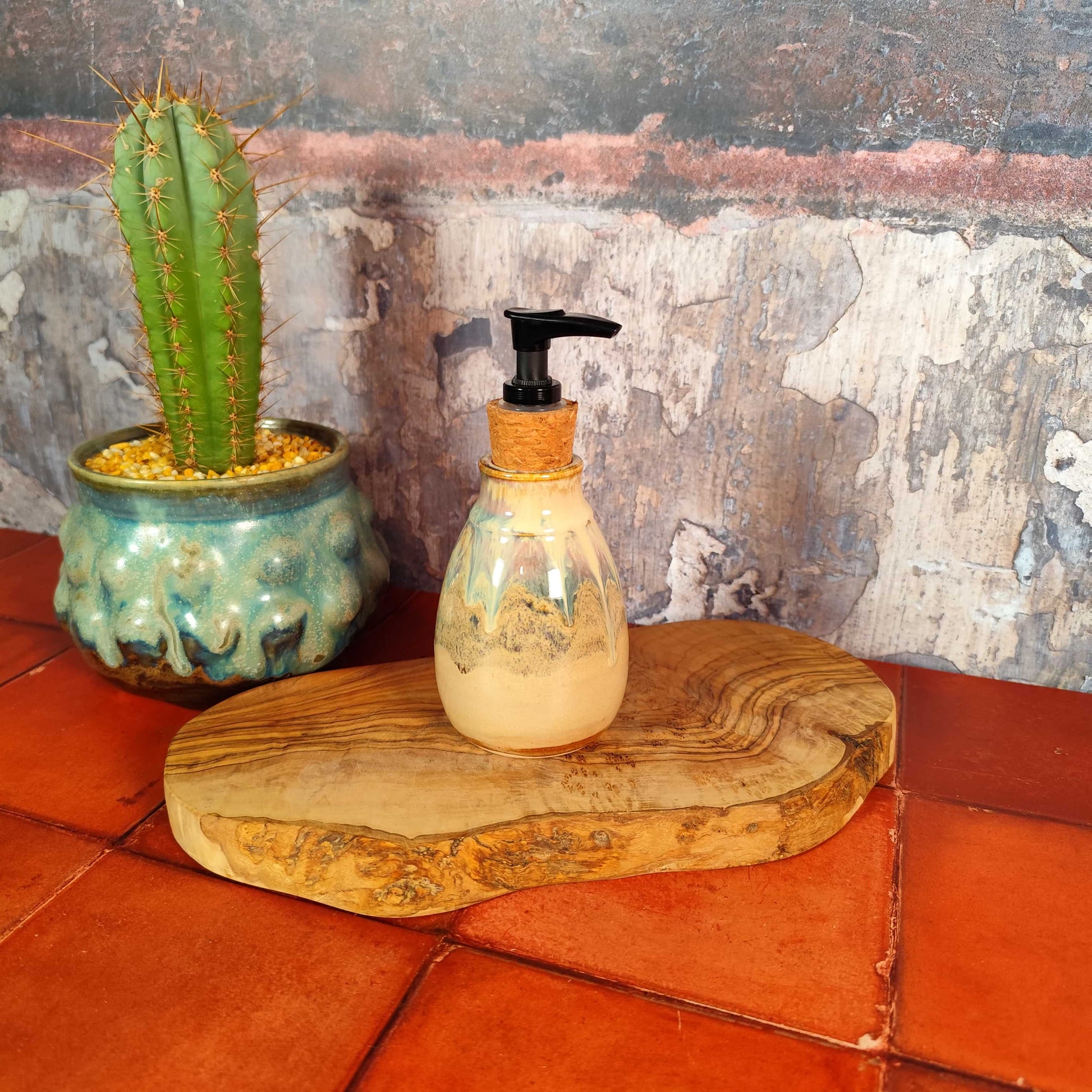 Decorative bottle with pump on a wooden board next to a cactus plant on a textured wall background. 