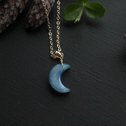 Blue crescent moon necklace on a dark surface with natural elements.